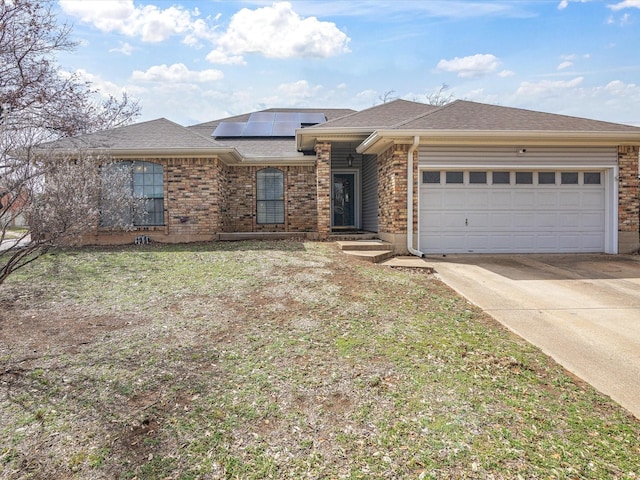 view of front facade featuring brick siding, roof with shingles, an attached garage, roof mounted solar panels, and driveway