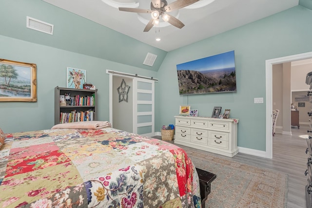 bedroom with lofted ceiling, a barn door, wood finished floors, visible vents, and baseboards