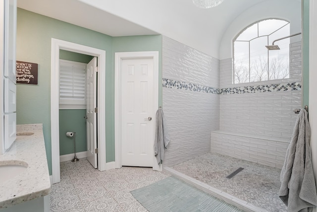 full bath with tile patterned flooring, a tile shower, vanity, and baseboards