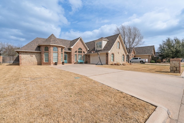 french country style house with a garage, brick siding, fence, driveway, and a front yard