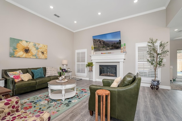 living area featuring baseboards, a glass covered fireplace, wood finished floors, and crown molding