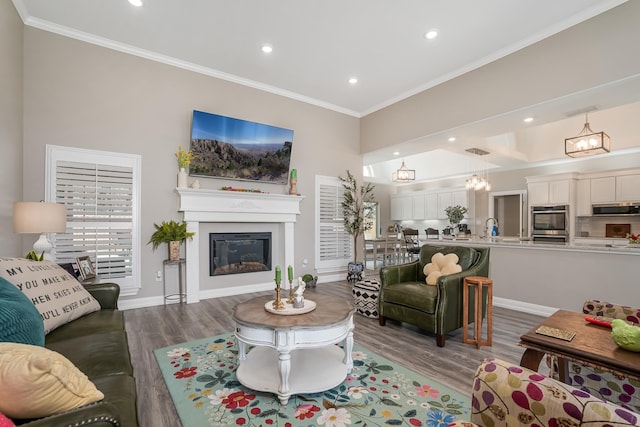 living area featuring baseboards, a glass covered fireplace, ornamental molding, wood finished floors, and recessed lighting