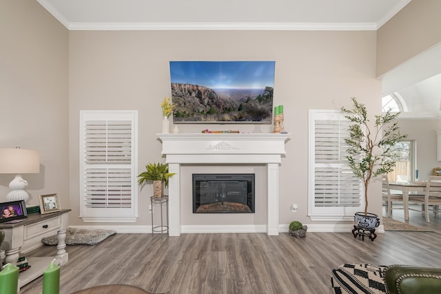 living area with ornamental molding, a glass covered fireplace, baseboards, and wood finished floors