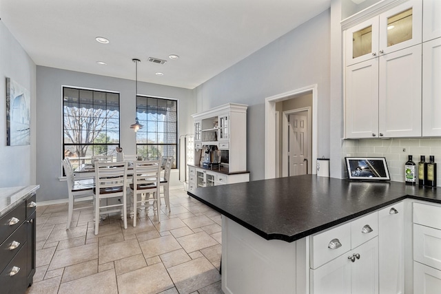 kitchen with tasteful backsplash, dark countertops, visible vents, white cabinets, and a peninsula