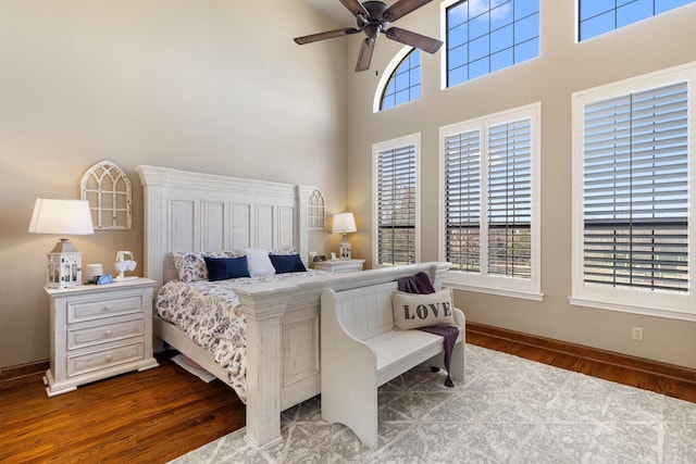 bedroom featuring a high ceiling, multiple windows, baseboards, and wood finished floors