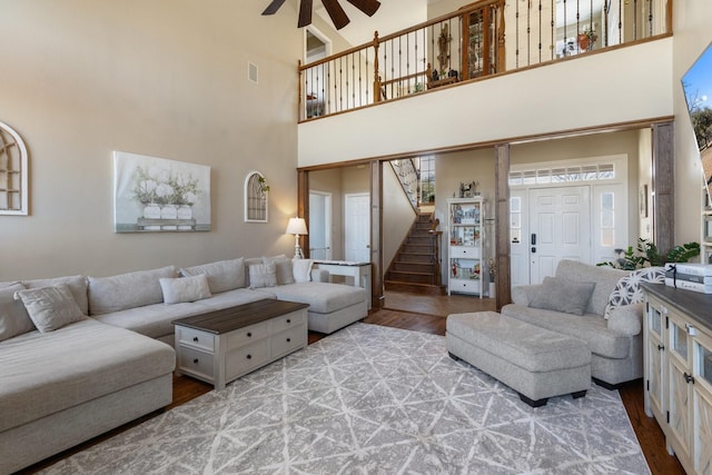 living area with wood finished floors, a towering ceiling, visible vents, stairs, and a ceiling fan