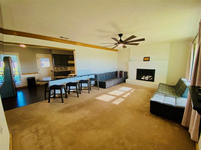 living area featuring carpet floors, visible vents, a ceiling fan, a glass covered fireplace, and a textured ceiling