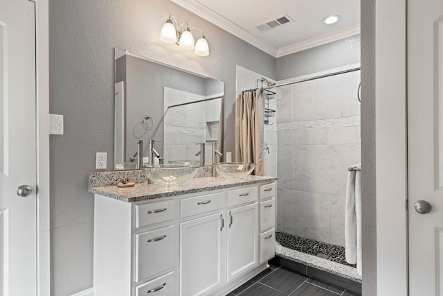 full bath featuring a sink, visible vents, a tile shower, and crown molding