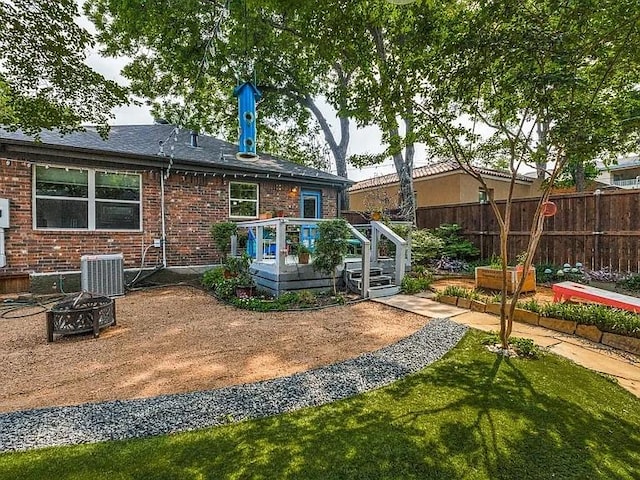 rear view of property with brick siding, central AC, fence, a fire pit, and a wooden deck