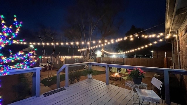 deck at twilight featuring an outdoor fire pit and fence