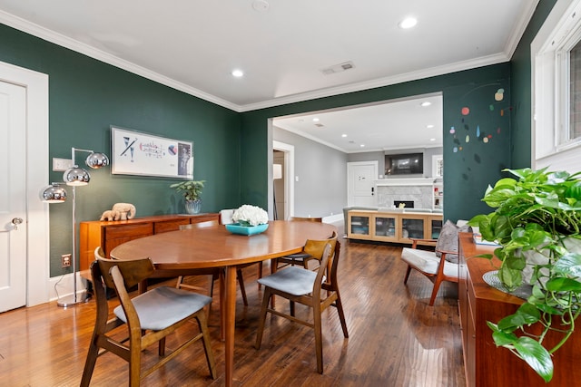 dining room with recessed lighting, a fireplace, wood finished floors, visible vents, and crown molding