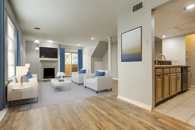 living area featuring a fireplace with raised hearth, recessed lighting, visible vents, baseboards, and light wood finished floors