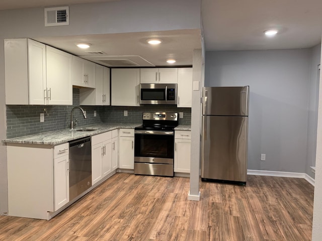 kitchen with visible vents, appliances with stainless steel finishes, light stone counters, wood finished floors, and a sink