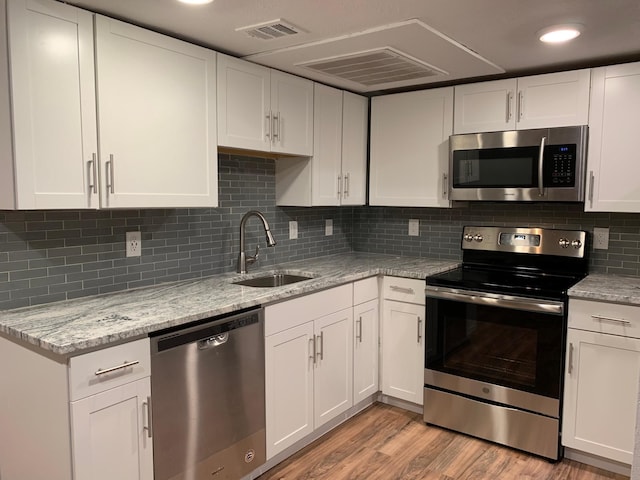 kitchen featuring visible vents, appliances with stainless steel finishes, light wood-style floors, white cabinetry, and a sink