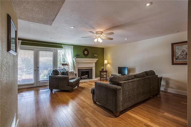 living room with a fireplace with raised hearth, light wood-style flooring, a ceiling fan, a textured ceiling, and baseboards