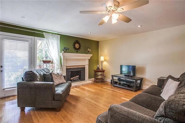 living area with a fireplace with raised hearth, plenty of natural light, wood finished floors, and baseboards