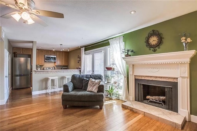 living area with visible vents, light wood-type flooring, a fireplace, and a ceiling fan