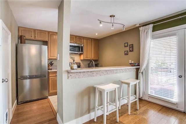 kitchen with a breakfast bar area, a sink, light countertops, appliances with stainless steel finishes, and light wood-type flooring