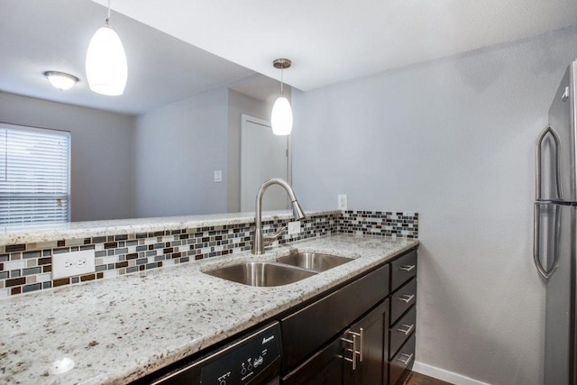 kitchen featuring a sink, hanging light fixtures, decorative backsplash, freestanding refrigerator, and light stone countertops