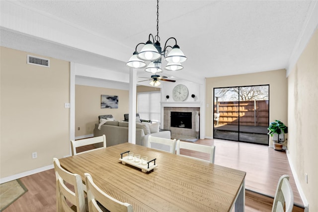 dining space with a textured ceiling, a tile fireplace, ceiling fan with notable chandelier, visible vents, and light wood-type flooring