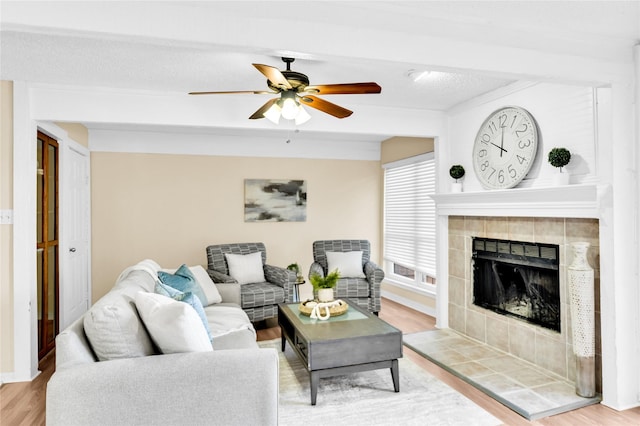 living room featuring a ceiling fan, baseboards, a tiled fireplace, and wood finished floors