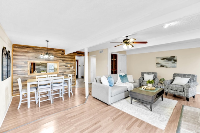 living area with an accent wall, wood walls, wood finished floors, visible vents, and beam ceiling