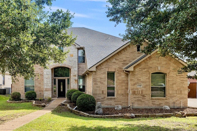 view of front of property featuring roof with shingles, central AC unit, a front lawn, and brick siding