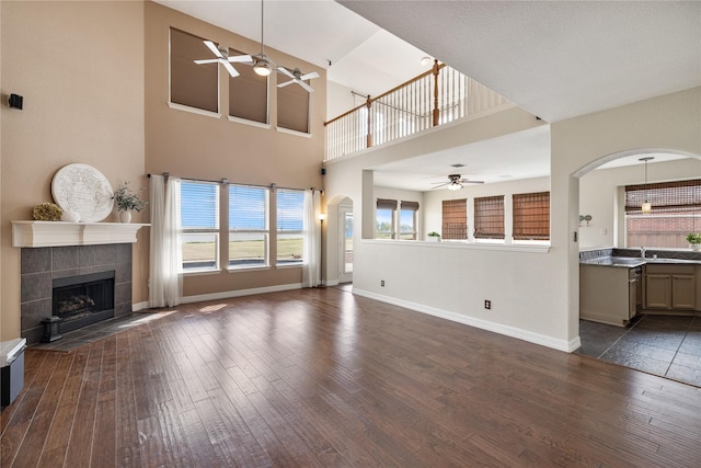 unfurnished living room featuring dark wood-style floors, a ceiling fan, a sink, a tile fireplace, and baseboards