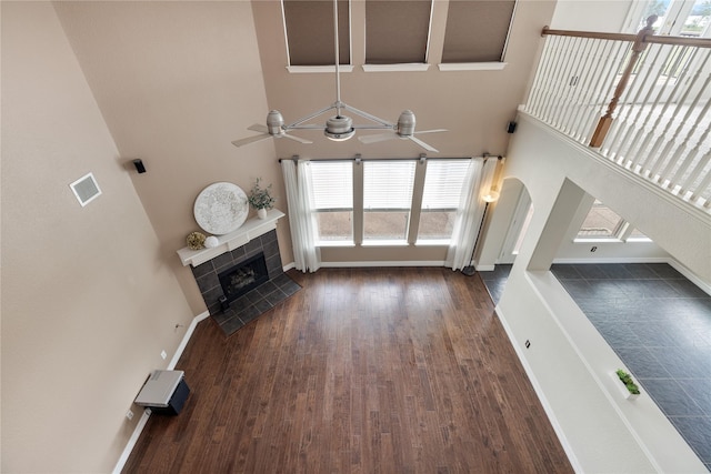 unfurnished living room with baseboards, visible vents, arched walkways, a tile fireplace, and dark wood-style floors