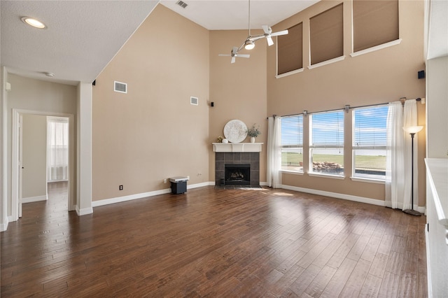 unfurnished living room with dark wood-style floors, a tiled fireplace, baseboards, and a healthy amount of sunlight