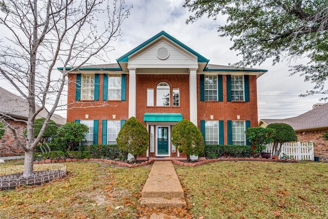 neoclassical / greek revival house featuring brick siding, a front yard, and fence