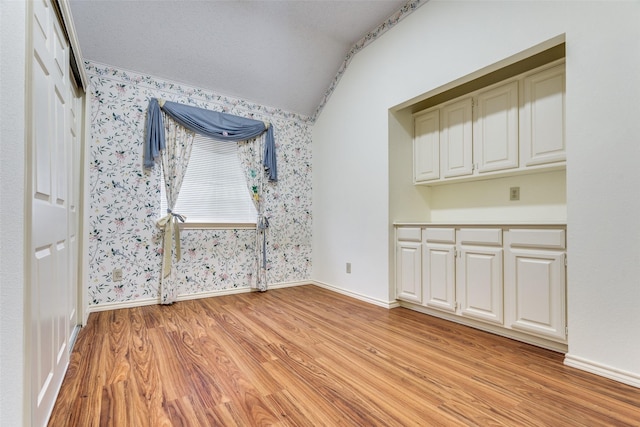 interior space featuring wallpapered walls, light wood-style flooring, baseboards, and vaulted ceiling