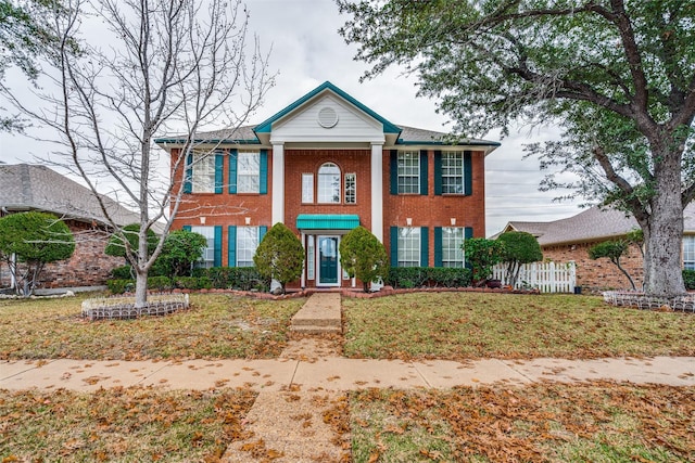 neoclassical / greek revival house with a front yard, fence, and brick siding