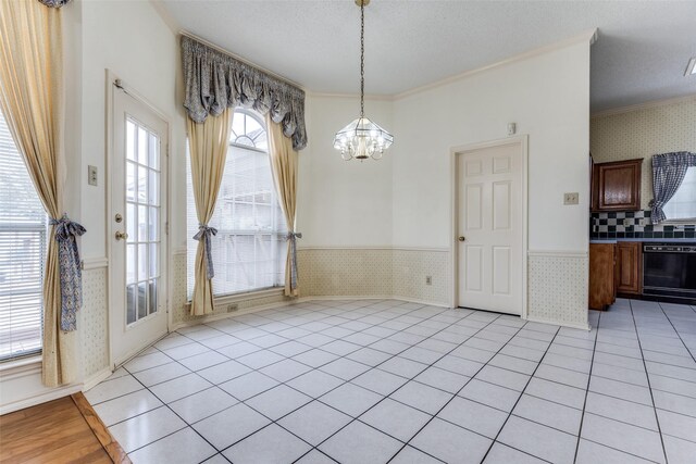 unfurnished dining area with a textured ceiling, ornamental molding, wainscoting, and light tile patterned floors