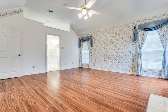 empty room featuring wallpapered walls, visible vents, lofted ceiling, wood finished floors, and a textured ceiling