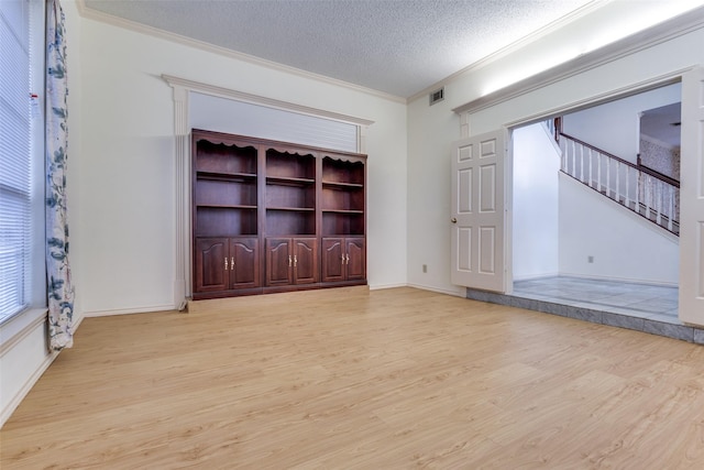 spare room with visible vents, stairway, ornamental molding, a textured ceiling, and light wood-type flooring