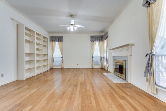 unfurnished living room featuring light wood-style flooring, a ceiling fan, baseboards, ornamental molding, and a tiled fireplace