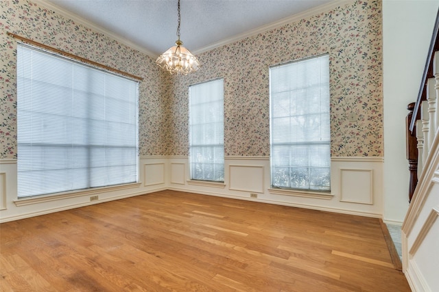 empty room with light wood-style floors, wainscoting, an inviting chandelier, and wallpapered walls