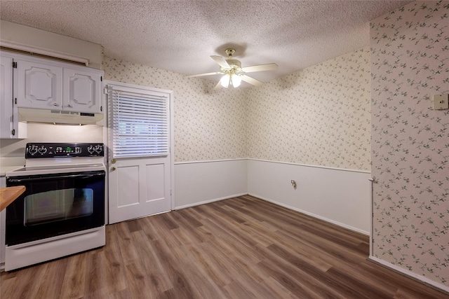 kitchen with a textured ceiling, under cabinet range hood, a wainscoted wall, electric range oven, and wallpapered walls