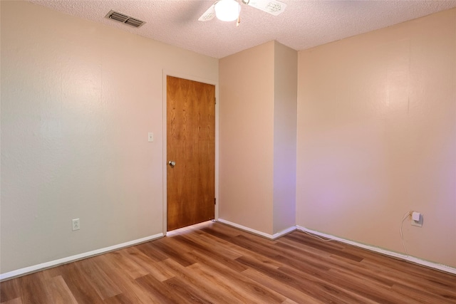 spare room with visible vents, a textured ceiling, baseboards, and wood finished floors