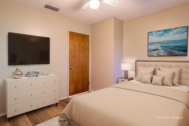 bedroom with baseboards, a textured ceiling, visible vents, and wood finished floors