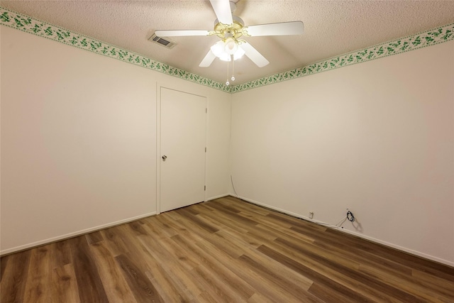 spare room with a textured ceiling, wood finished floors, visible vents, baseboards, and a ceiling fan