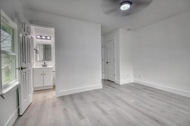 unfurnished bedroom featuring light wood-type flooring, a sink, baseboards, and connected bathroom