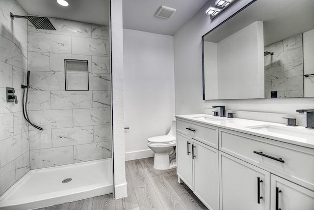 full bath featuring a tile shower, wood finished floors, and a sink