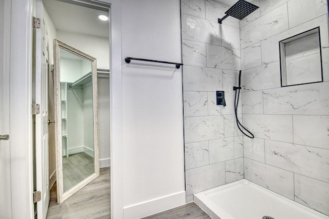 bathroom featuring wood finished floors, a tile shower, and baseboards