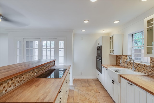 kitchen with a sink, wood counters, backsplash, black appliances, and crown molding