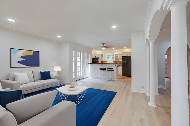 living area featuring ornamental molding, arched walkways, light wood-style flooring, and ornate columns