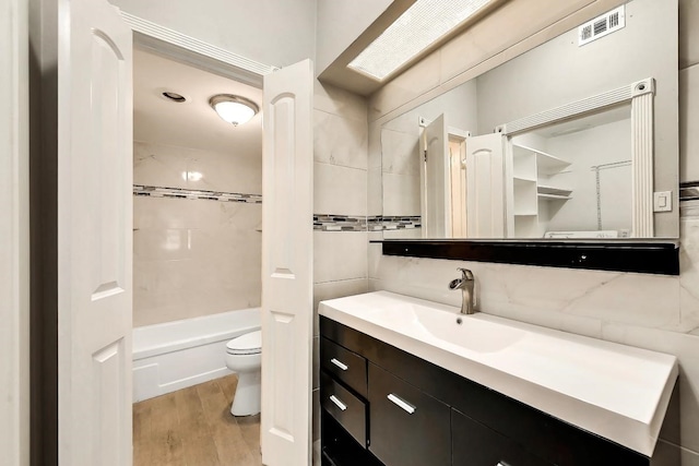 full bath with toilet, wood finished floors, vanity, visible vents, and tile walls