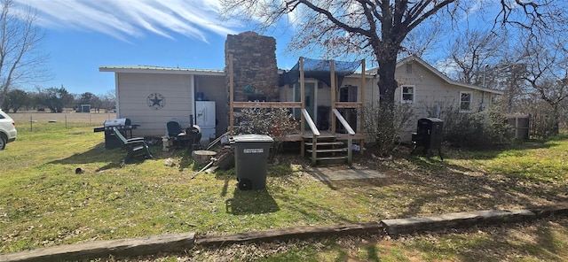 rear view of house featuring a chimney, fence, metal roof, and a lawn