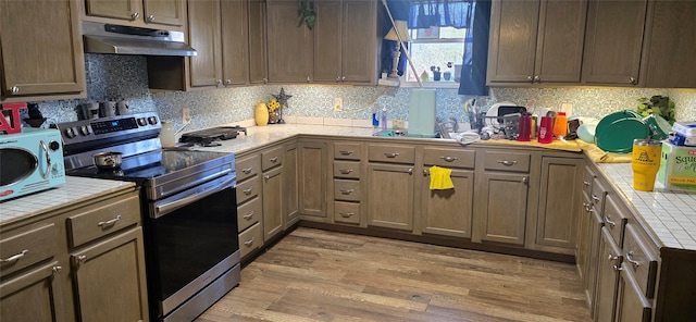 kitchen with tile countertops, under cabinet range hood, light wood-style floors, and electric stove